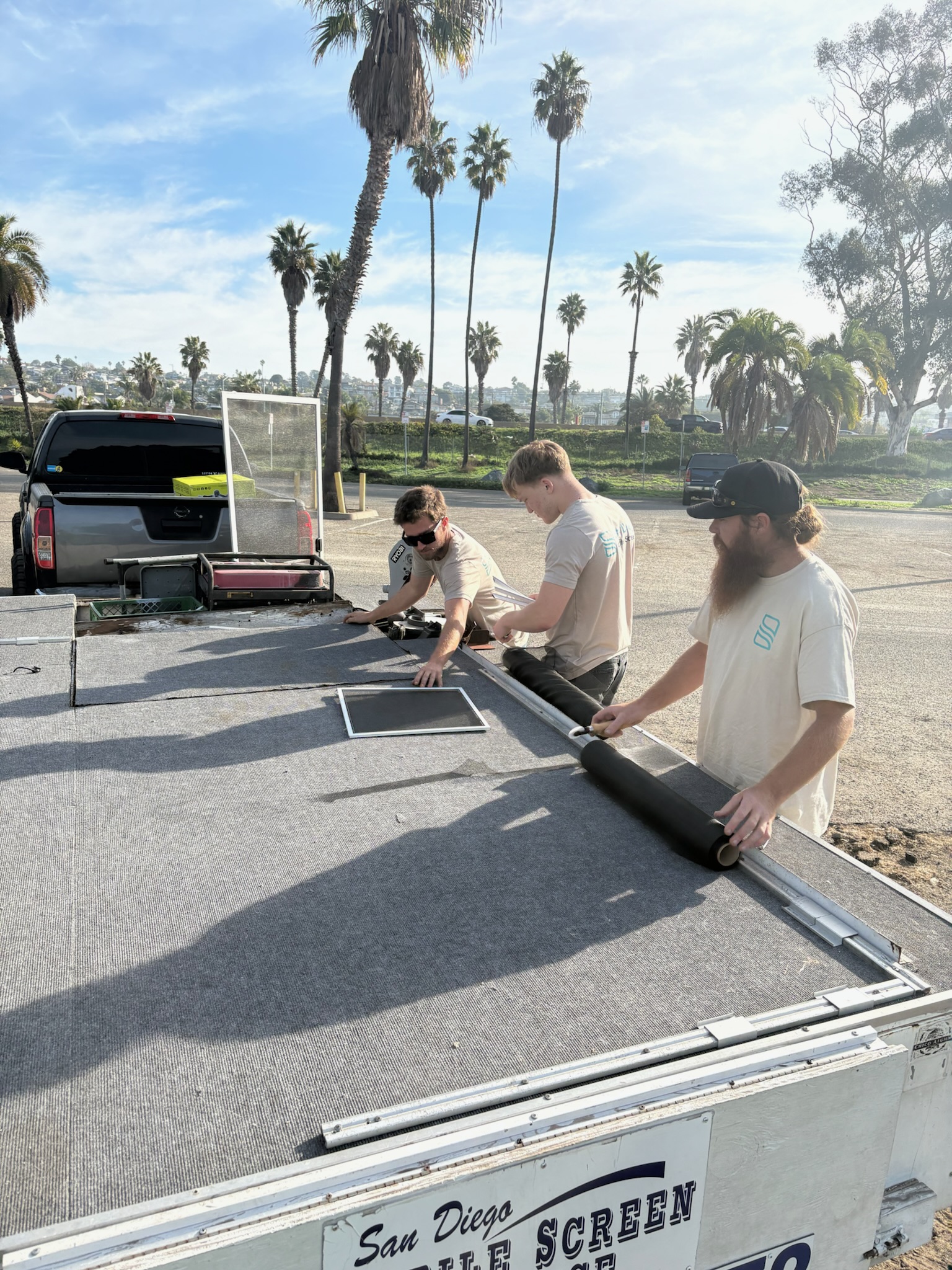 Technicians building a custom screen on the mobile workshop trailer with palm trees in background